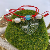 Hermoso set de 2 pulseras confeccionadas a mano con charm de acrílico en forma de corazón dividido con la palabra Best Friends y montadas en hilo de nylon ajustable. Además también incluyen una perla original de agua dulce y un cuarzo ágata. Excelente joyería para regalar a tu mejores amig@s. Este set tiene un bello y único estilo para hacerlas lucir únicas y más unidas. Sus separadores plateados son en  baño en plata u oro.  Resistentes al agua.